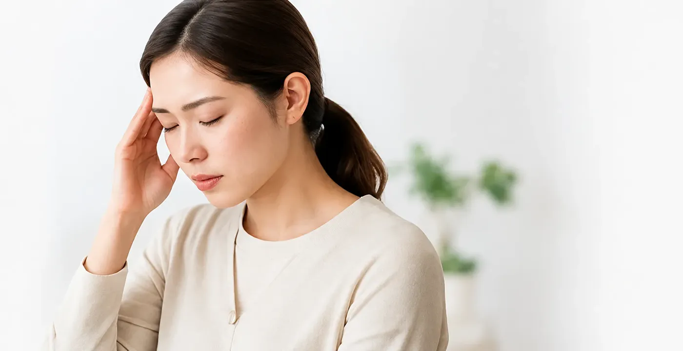 こめかみに手を当て、頭痛に悩む女性