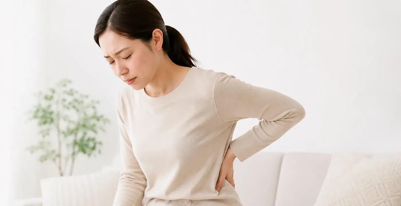 腰に手を当て、腰のつらさを感じている女性